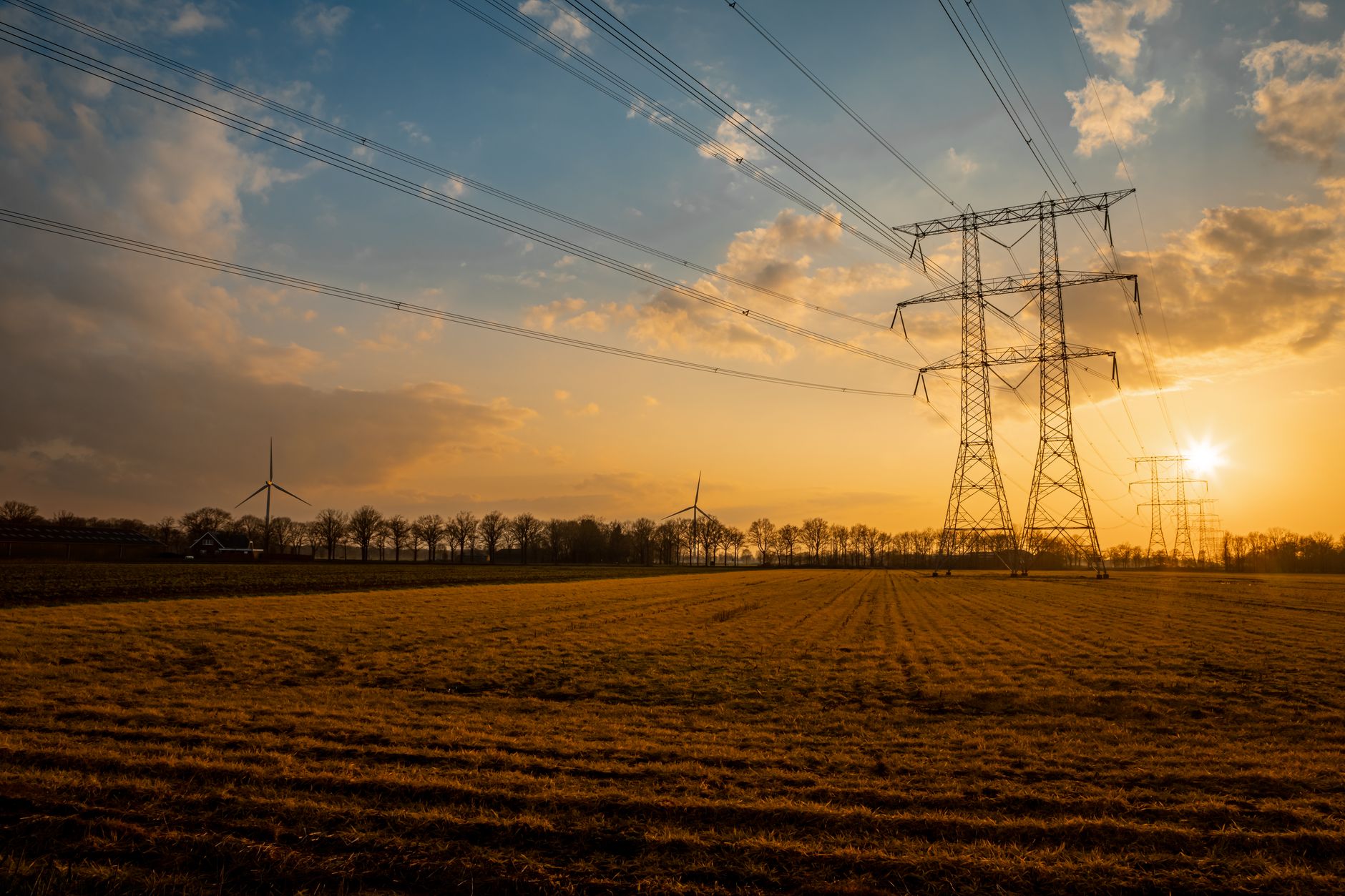 Hoogspanningsmasten en windturbines boven een akker bij zonsondergang, illustratief bij de netcapaciteit voor woningbouw