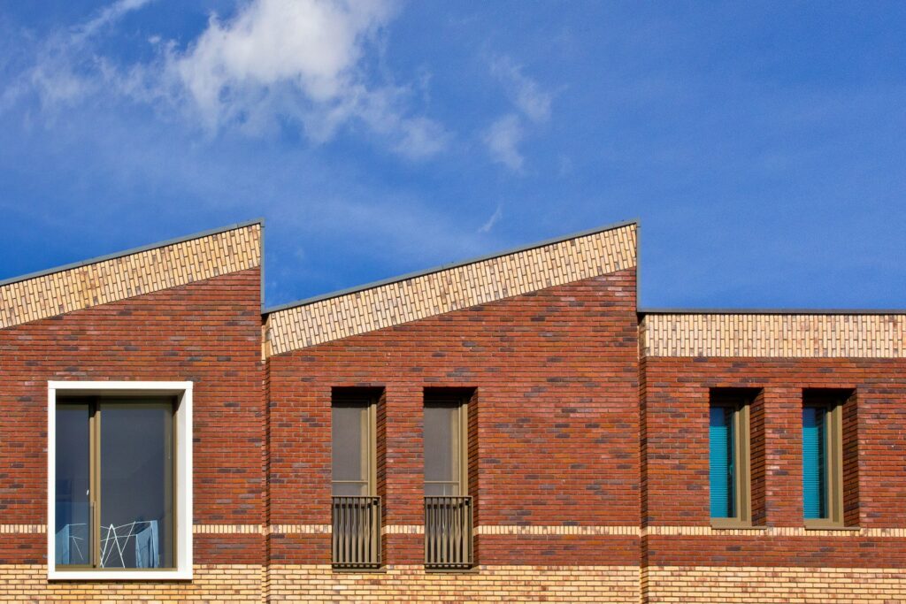 Gevel van nieuwbouwwoningen in rode baksteen met schuine daklijnen onder een blauwe lucht