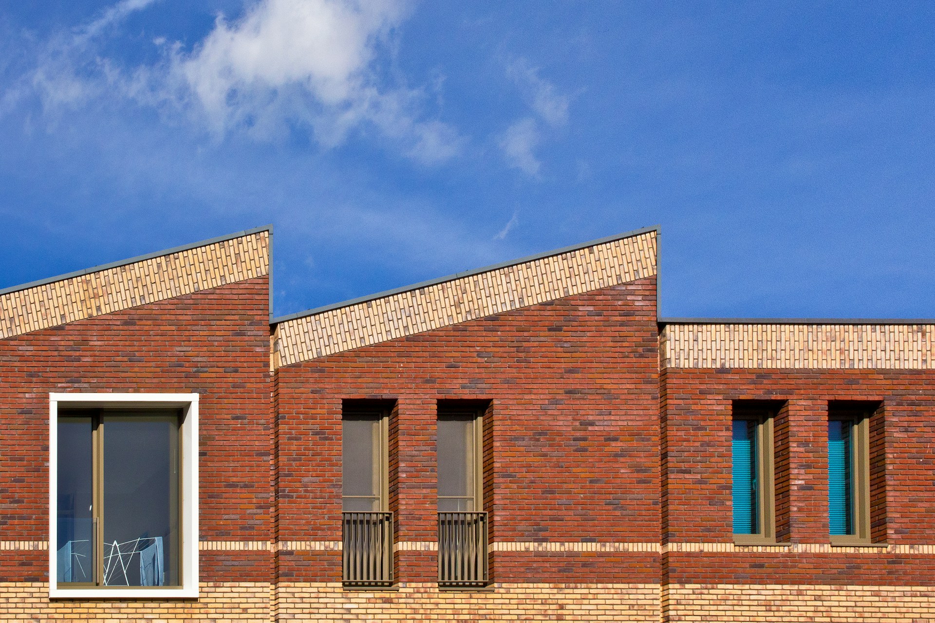 Gevel van nieuwbouwwoningen in rode baksteen met schuine daklijnen onder een blauwe lucht