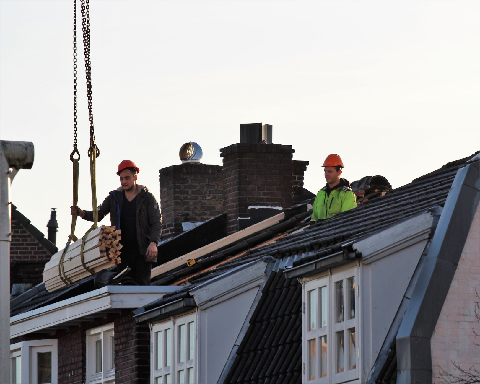 Bouwvakkers op een dak met een hijslast, illustratief bij de woningbouw in Enschede aan de Telgendijk