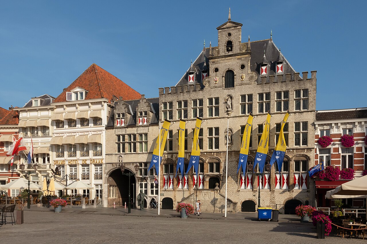 Het stadhuis van Bergen op Zoom aan de Grote Markt met gele vlaggen, naast Hotel De Draak, onder een blauwe lucht