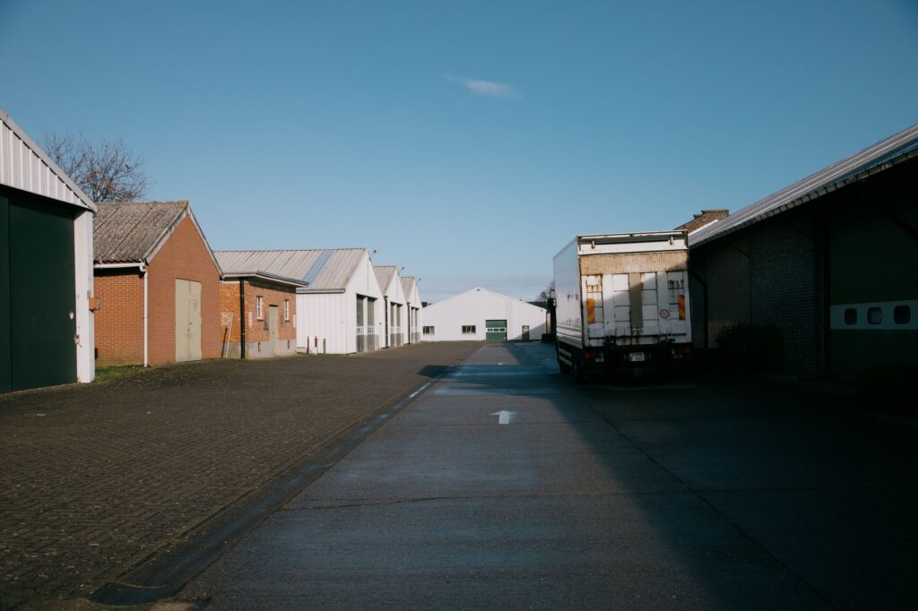 Rij logistieke hallen en bedrijfspanden langs een bedrijfsweg met een geparkeerde vrachtwagen onder blauwe lucht