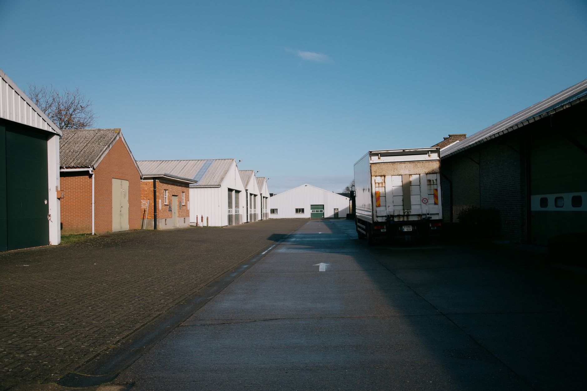 Rij logistieke hallen en bedrijfspanden langs een bedrijfsweg met een geparkeerde vrachtwagen onder blauwe lucht