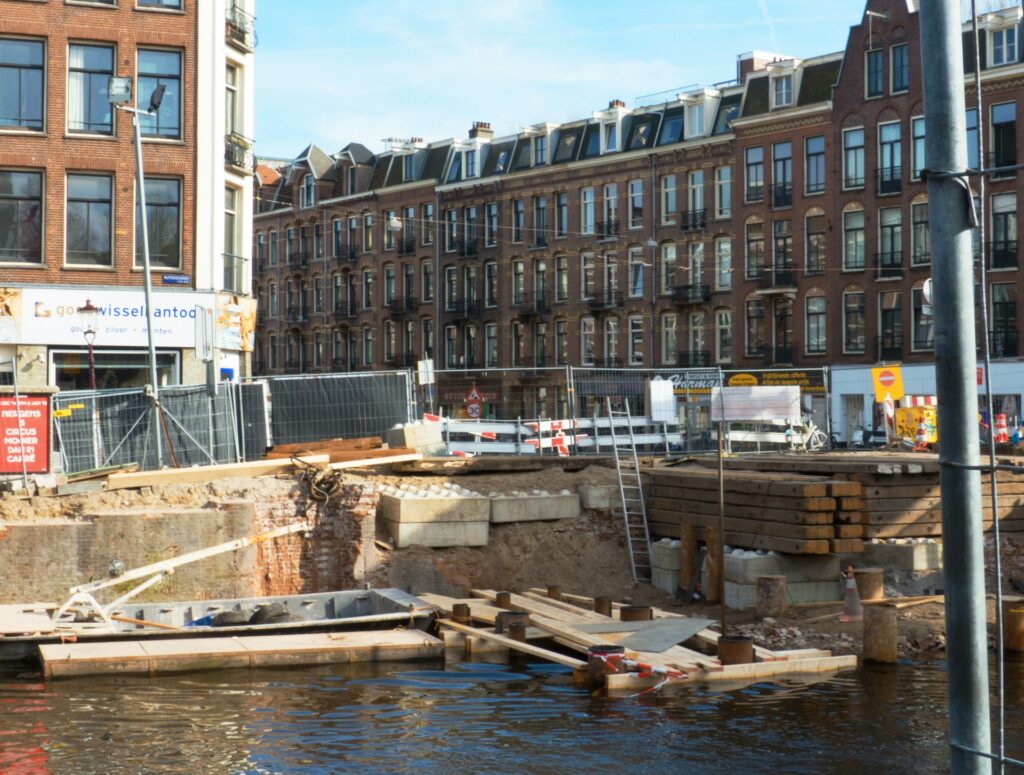 Bouwwerkzaamheden aan een kademuur langs een Amsterdamse gracht met woningen op de achtergrond