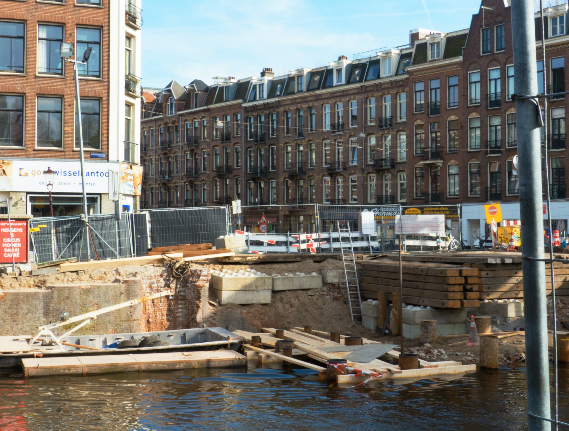 Bouwwerkzaamheden aan een kademuur langs een Amsterdamse gracht met woningen op de achtergrond