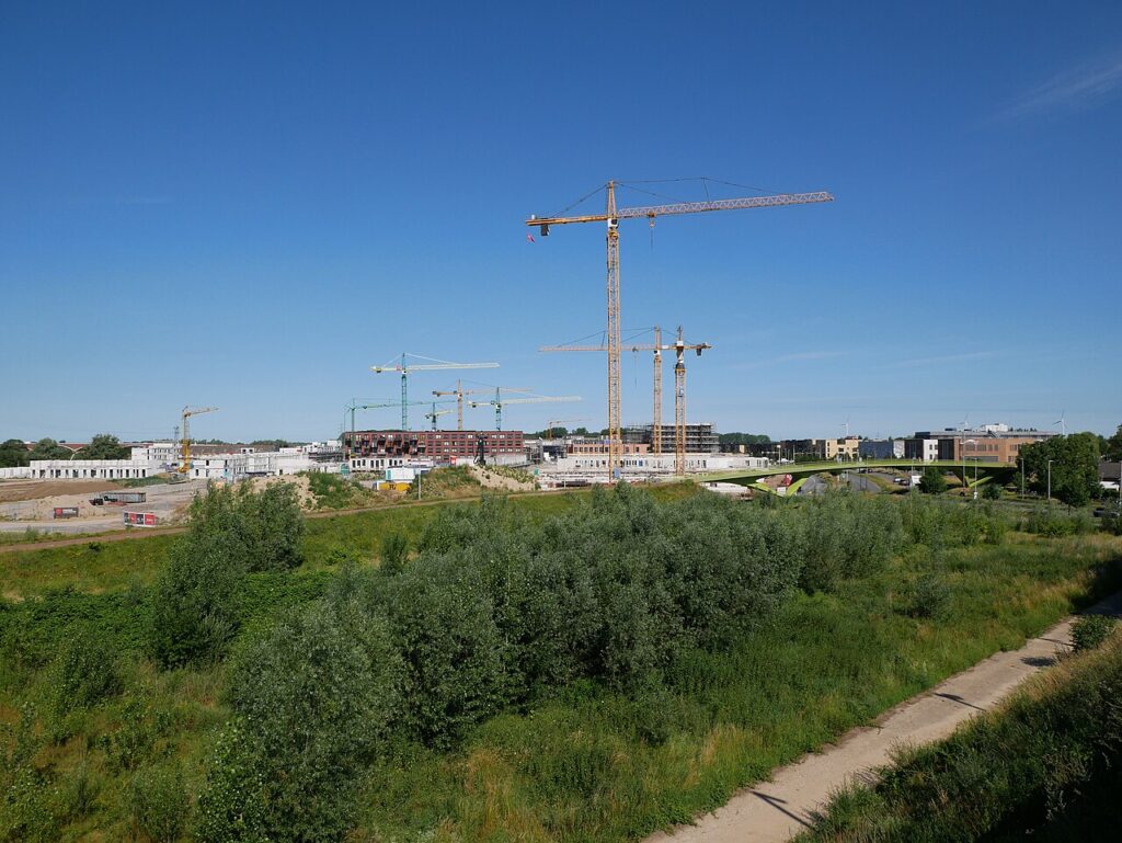 Nederlandse nieuwbouwwijk in aanbouw met meerdere bouwkranen boven appartementen en rijwoningen