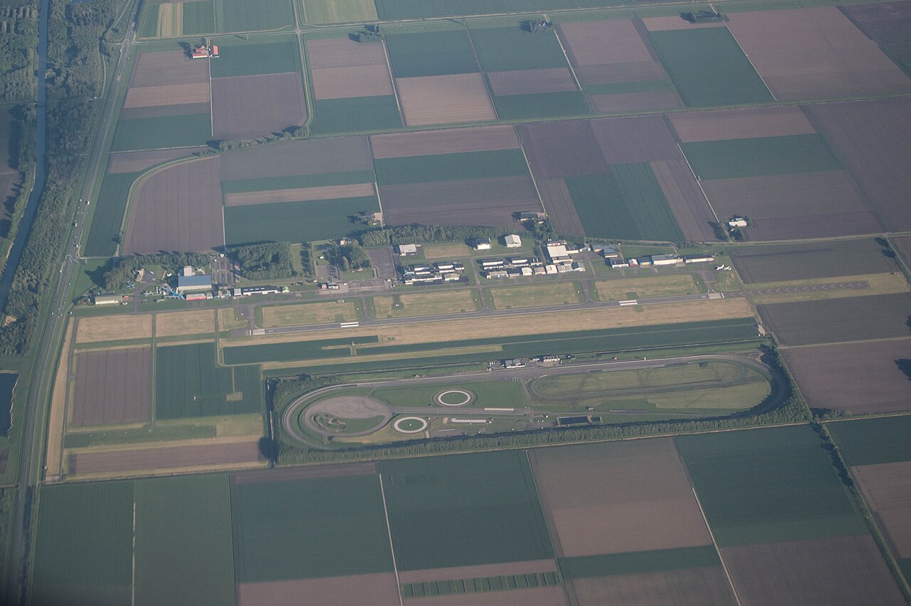 Luchtfoto van Lelystad Airport met de start- en landingsbaan, het circuit en omliggende akkers