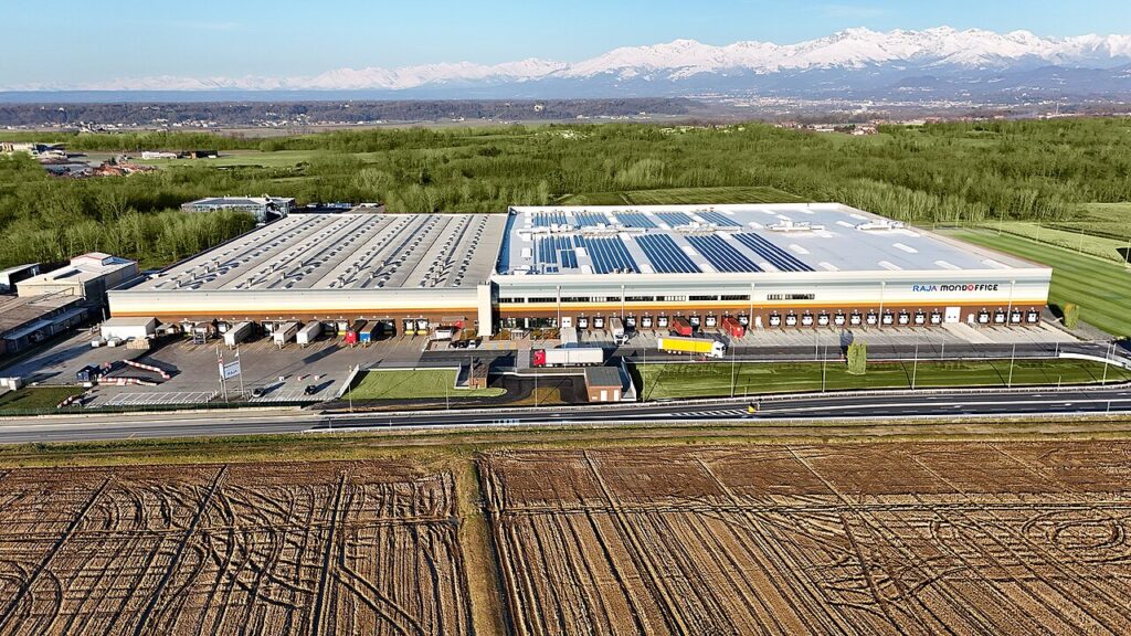 Luchtfoto van een groot distributiecentrum met zonnepanelen in Italië, met besneeuwde Alpen op de achtergrond