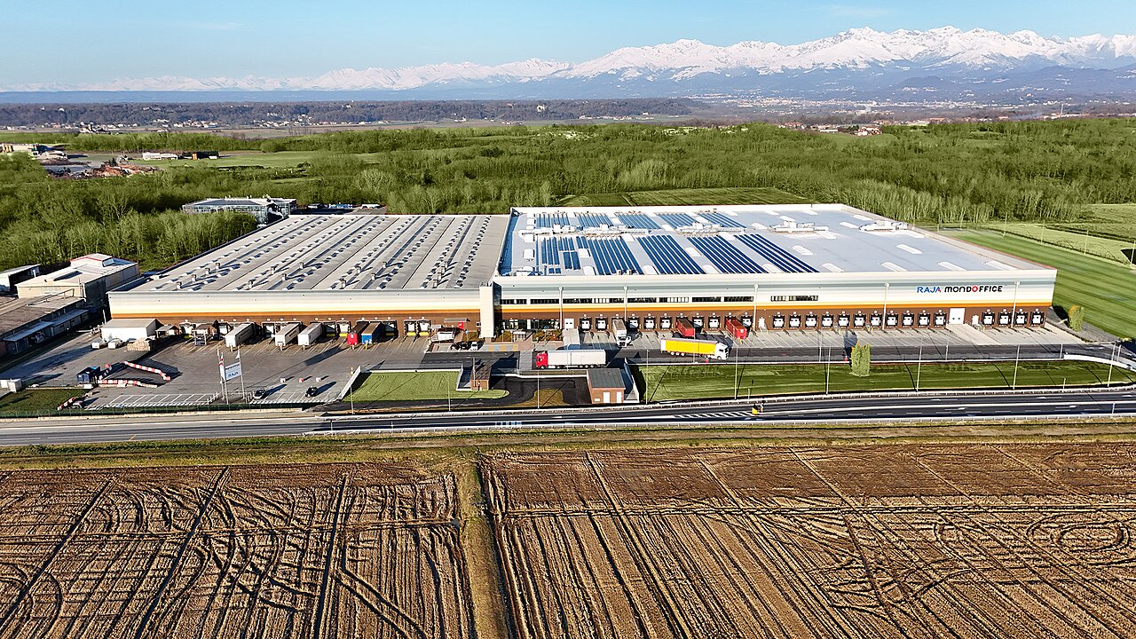 Luchtfoto van een groot distributiecentrum met zonnepanelen in Italië, met besneeuwde Alpen op de achtergrond