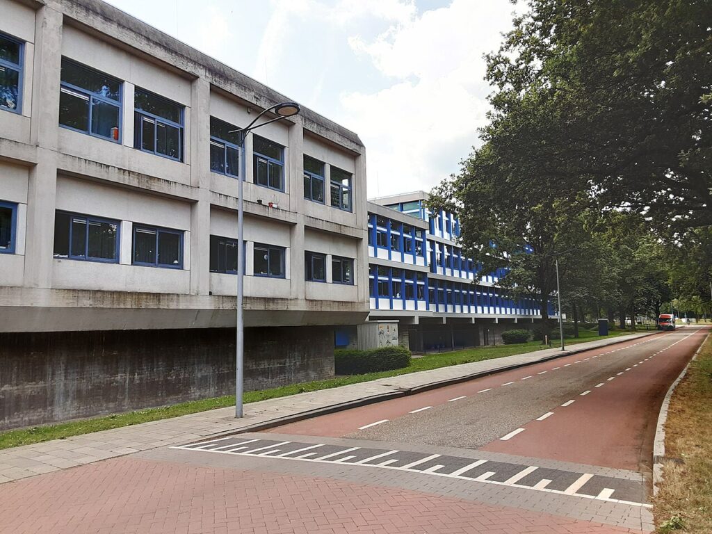 Betonnen kantoorgebouw met blauwe kozijnen langs een weg met fietspad aan de Schepersmaat in Assen