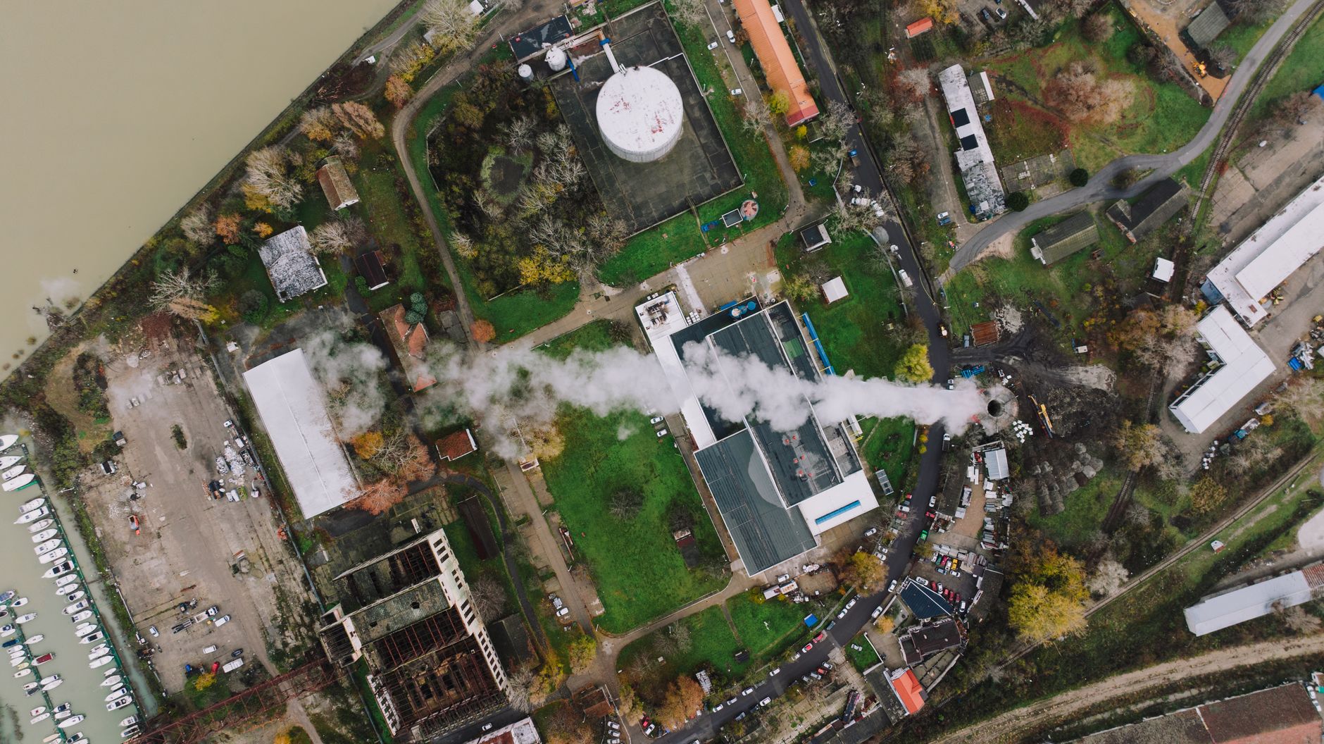 Luchtfoto van een bedrijf met rookpluim tussen woningen, illustratief bij toezicht onder de Omgevingswet