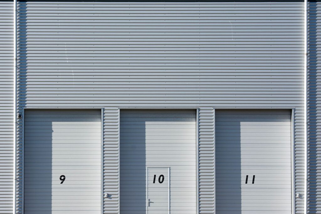 Gevel van een bedrijfsverzamelgebouw met drie genummerde witte overheaddeuren in grijze metalen beplating