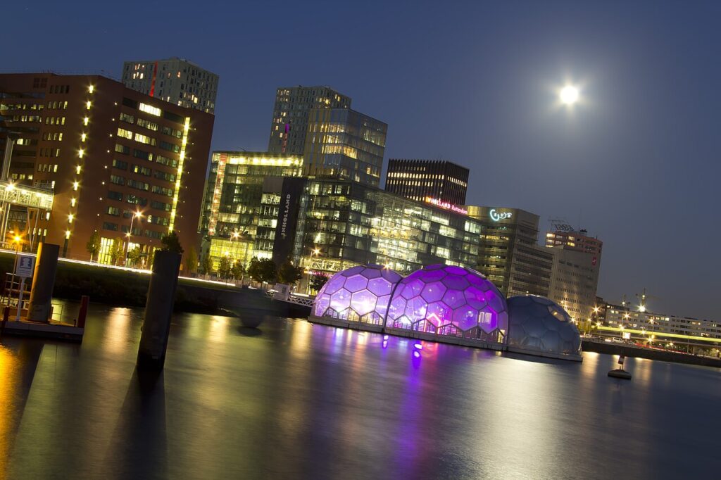 Verlichte kantoortorens aan de Rijnhaven op de Kop van Zuid in Rotterdam bij avond, met de drijvende paviljoens op het water