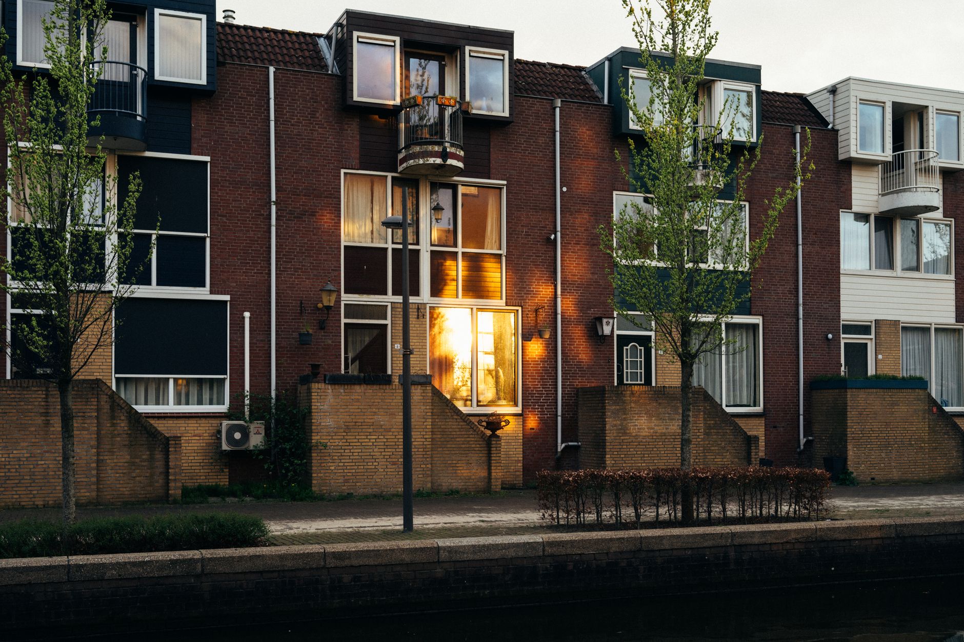 Rij eengezinswoningen met voortuinen aan een gracht in Almere bij zonsondergang